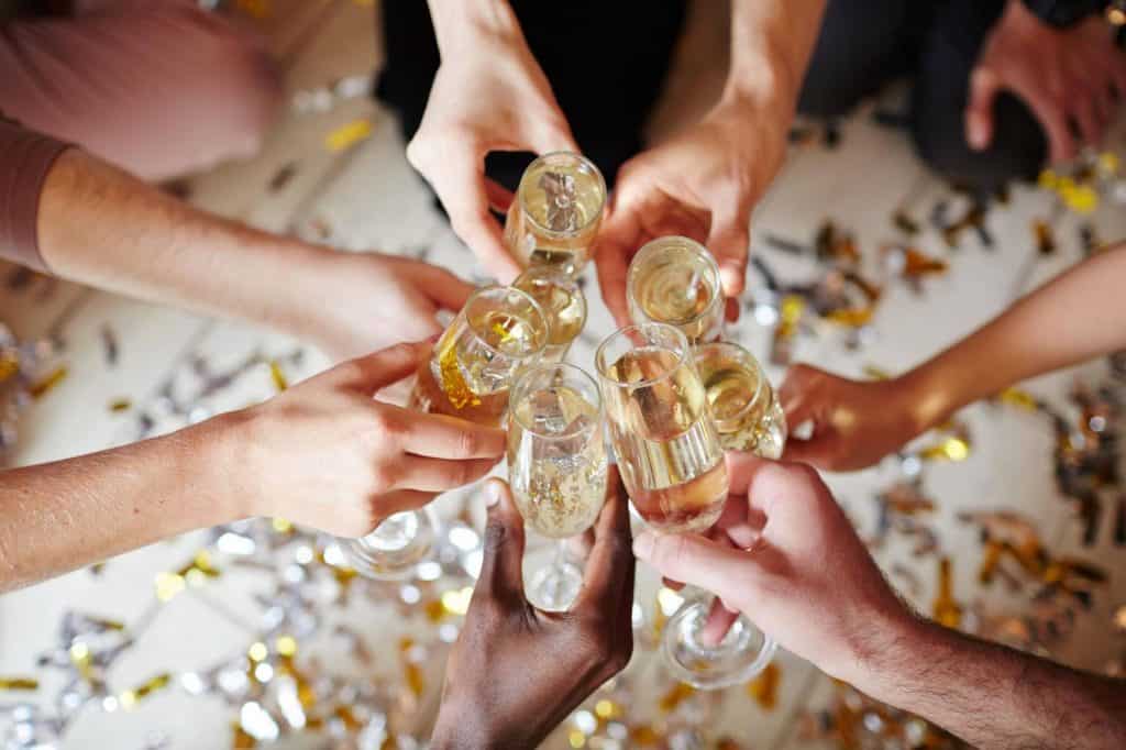 Butelki z szampanem w rękach ludzi na uroczystości ślubnej lub imprezie, świętowanie, radosne chwile, towarzyska atmosfera, motyw celebracji, zdjęcie z góry, zbliżenie, festyn.