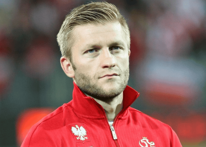 Fotografia sportowca w czerwonej koszulce z orłem, mecz piłki nożnej, profesjonalny zawodnik, sportsmen na boisku, drużyna narodowa, sport i rekreacja, Polska, rozgrywki piłkarskie, kibice, atmosfera na stadionie.