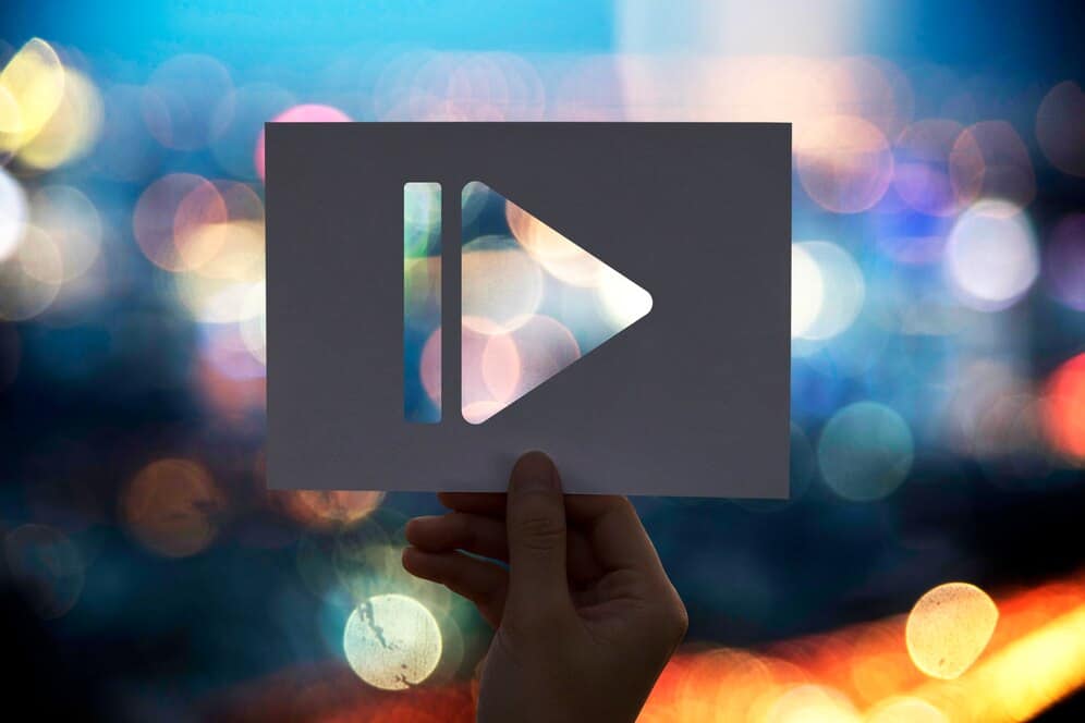 Plakat z symbolem odtwarzania video lub multimediów, na tle rozmytego miejskiego światła nocnego.