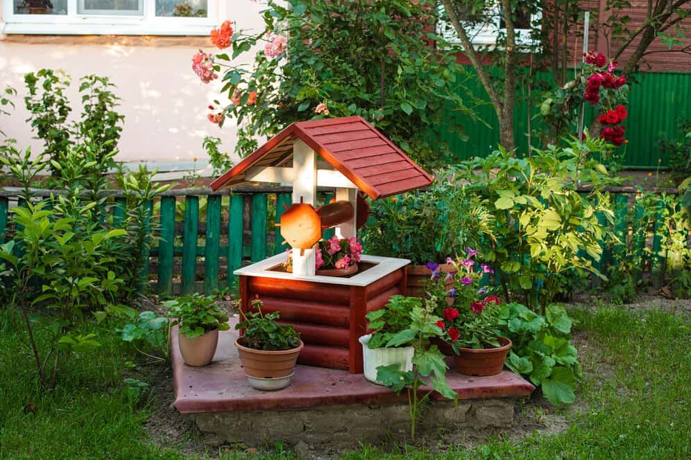 Zewnętrzny omlnik na ogród z roślinami i kwiatami, element małej architektury ogrodowej, dekoracja ogrodu, przydomowa rabata z kwiatami i zaaranżowana przestrzeń, ogród przy domu.