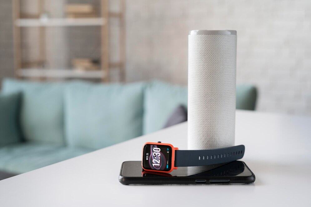 Nowoczesny głośnik smart speaker na stole w domu z opaską fitness i smartfonem, technologia do domu i ogrodu, inteligentny sprzęt audio i wearables, wygodny i stylowy wystrój wnętrz, innowacyjne urządzenia elektroniczne.