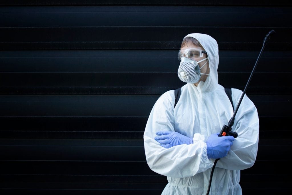 Ochrona osobista i dezynfekcja, osoba w maseczce i kombinezonie ochronnym, spray do dezynfekcji, profilaktyka w domu i ogrodzie, dekoracje i zabezpieczenia, troska o zdrowie i bezpieczeństwo w domu i ogrodzie.