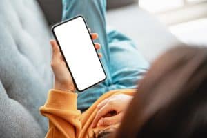Młoda kobieta leży na kanapie i przegląda telefon