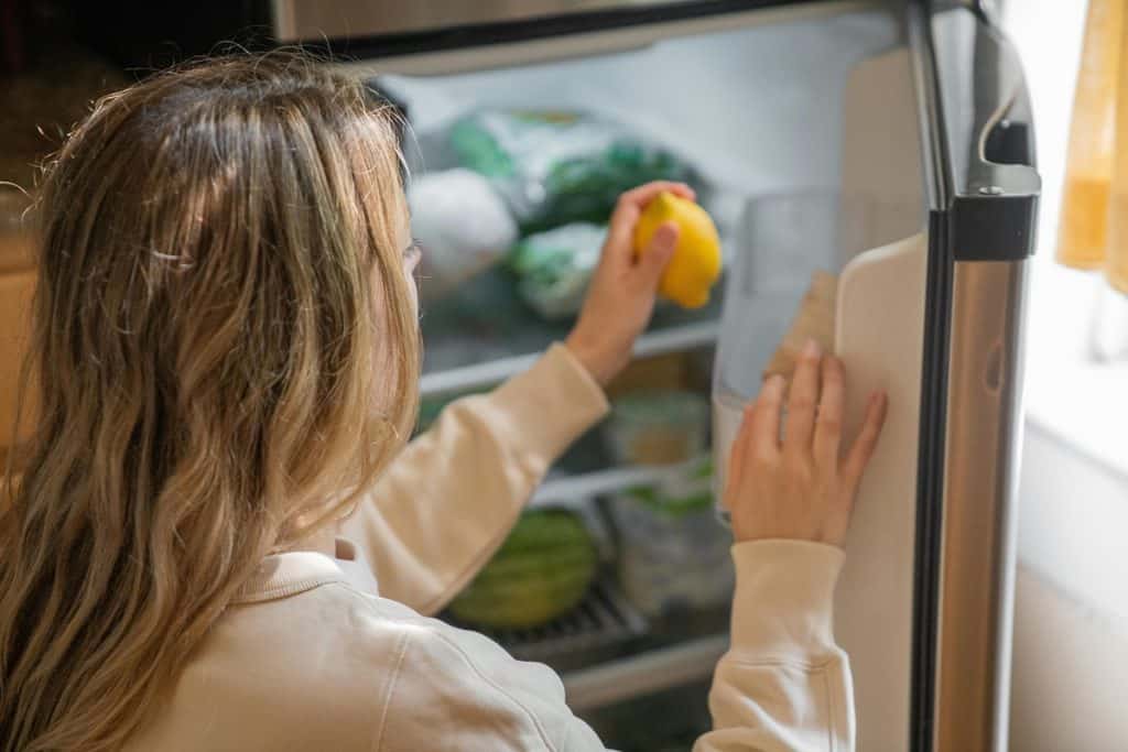 Świeży lemon w lodówce, kobieta sięga po produkty spożywcze, kuchnia domowa, codzienne zakupy, zdrowa żywność, wygoda i funkcjonalność, aranżacja wnętrza.