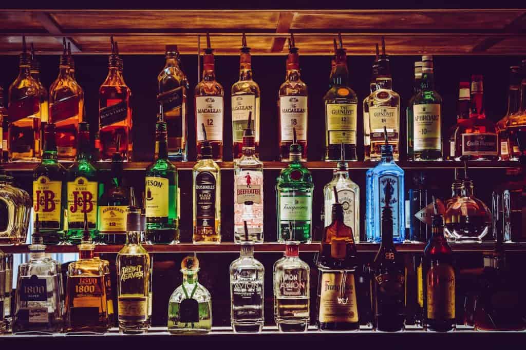 Szklana półka z szerokim wyborem alkoholi i whiskey, podświetlona od tyłu, elegancka aranżacja na barze lub w sklepie z alkoholami, idealna do promocji win i mocnych trunków.